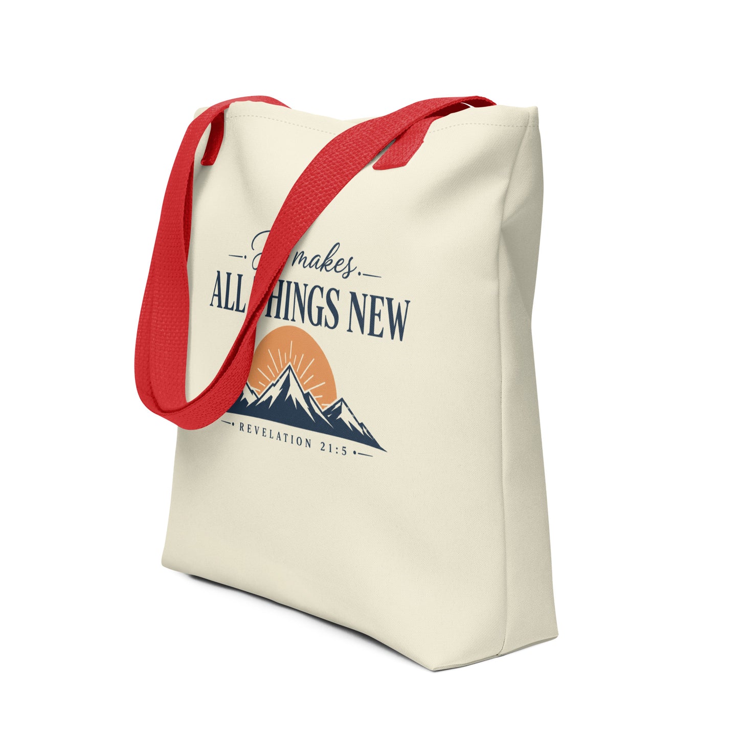 Angled view of a Christian tote bag featuring red straps, a neutral cream background, mountain and sunrise artwork, and “He Makes All Things New” lettering.