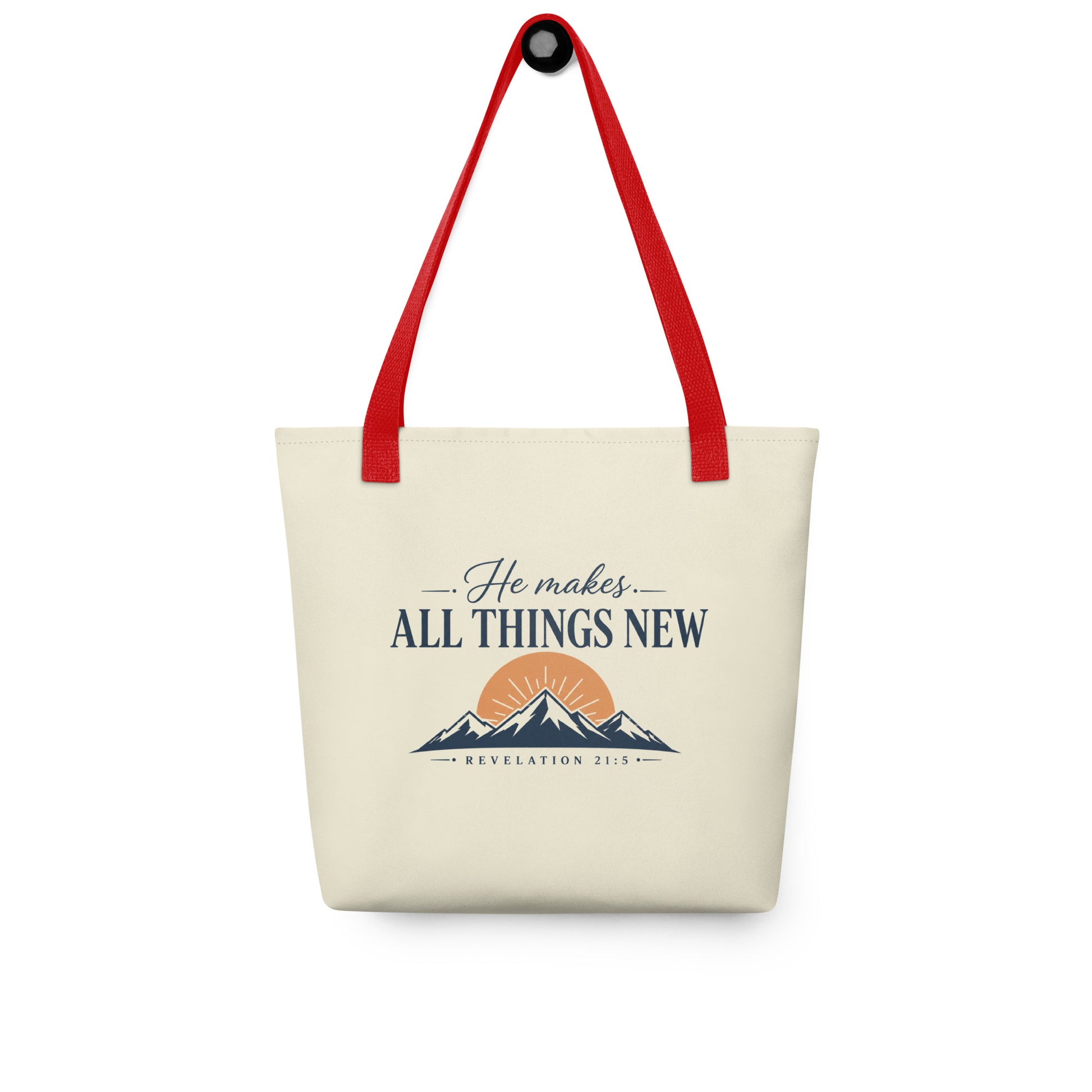 Christian tote bag hanging on a hook, featuring red straps, a cream body, mountain artwork, and “He Makes All Things New” text.