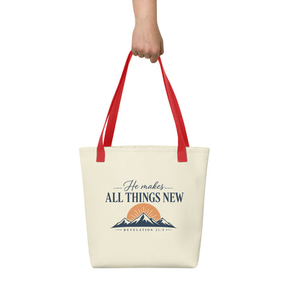 Person holding a cream Christian tote bag with red handles, a mountain sunrise design, and the Bible verse reference Revelation 21:5.