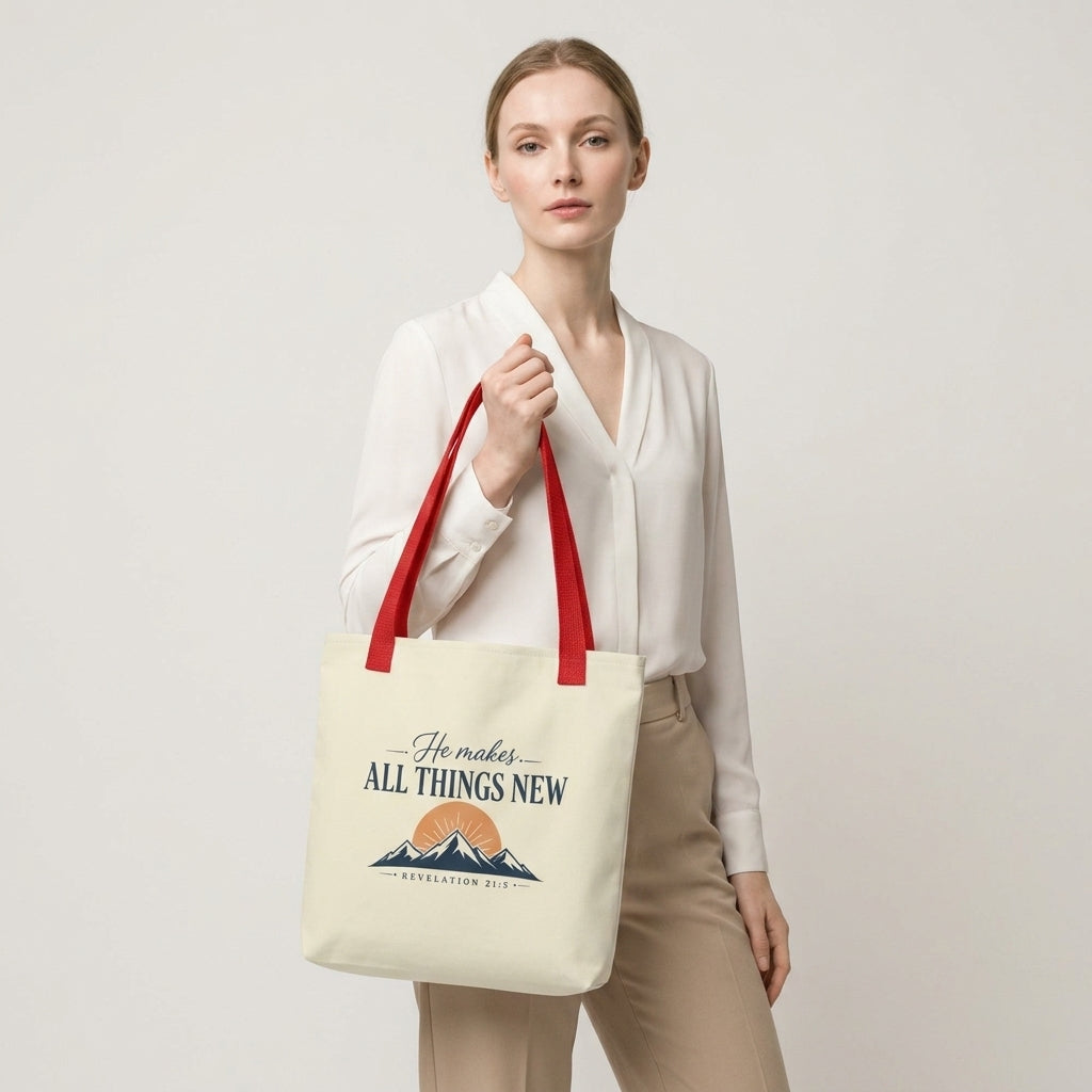 Model carrying a cream Christian tote bag with red handles and a faith-inspired mountain design featuring Revelation 21:5.