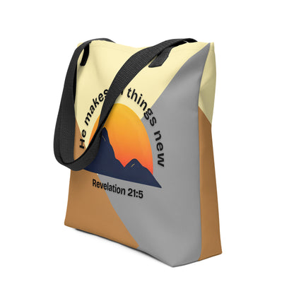 Angled view of the color-block tote with black handles, showing the curved “He makes all things new” text around a sunset-and-mountain design and the verse reference “Revelation 21:5.”