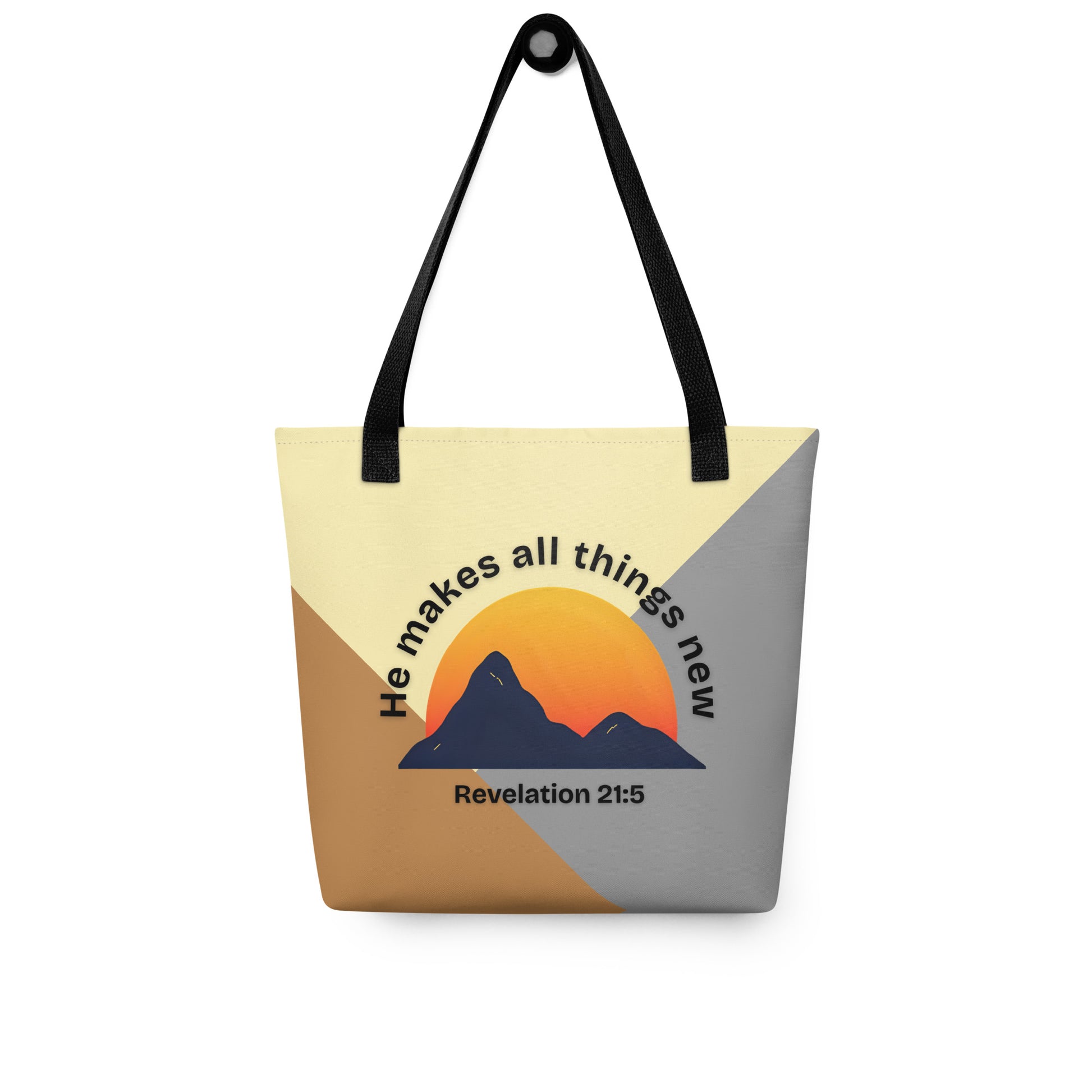 Color-block Christian tote bag with black straps hanging on a hook, displaying a mountain silhouette over an orange sun with “He makes all things new” and “Revelation 21:5.”