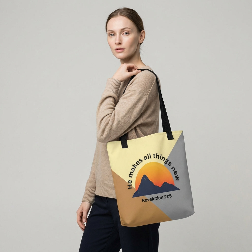 Model carrying a black-strap tote with a modern color-block design, featuring a mountain sunset graphic and the message “He makes all things new” (Revelation 21:5) on the front.