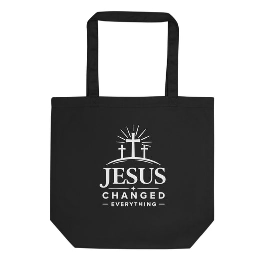 Front view of a black cotton Christian tote bag with matching black handles and a white “Jesus Changed Everything” cross design.
