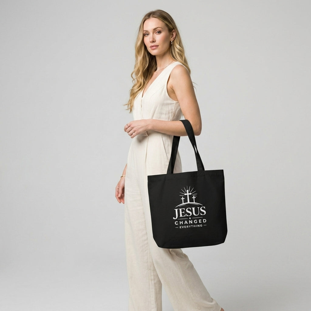 Model carrying a black cotton Christian tote bag with a white faith-based “Jesus Changed Everything” design.