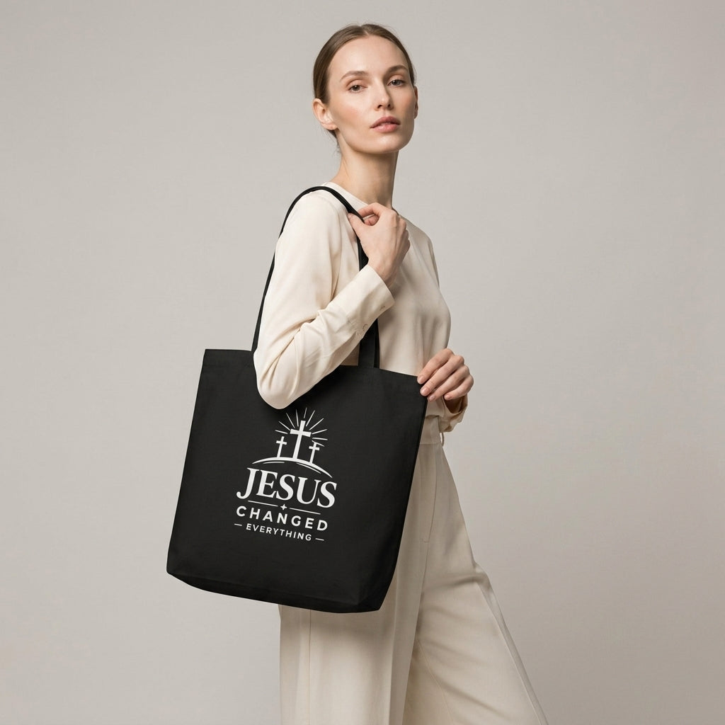 Model carrying a black cotton Christian tote bag with a white faith-based “Jesus Changed Everything” design.
