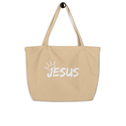 Large natural cotton tote bag hanging on a hook featuring a white “JESUS” design with a crown graphic above it.