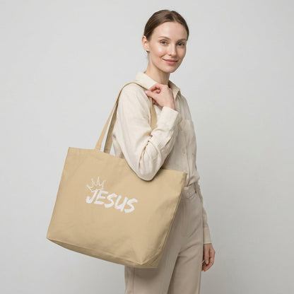 Model holding a large natural cotton tote bag with a white “JESUS” graphic and crown detail on the front.
