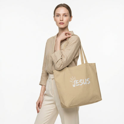 Model holding a large natural cotton tote bag with a white “JESUS” graphic and crown detail on the front.