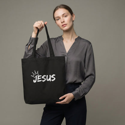 Model holding a black cotton tote bag with a white “JESUS” graphic and crown detail on the front.