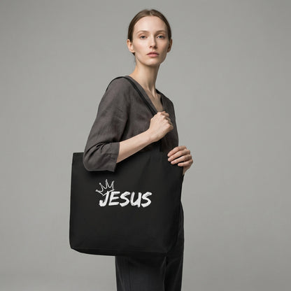 Model holding a black cotton tote bag with a white “JESUS” graphic and crown detail on the front.