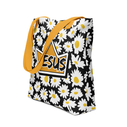 Angled view of the black floral tote with yellow handles, showing the white daisy pattern and the crown-shaped “JESUS” design centered on the front.