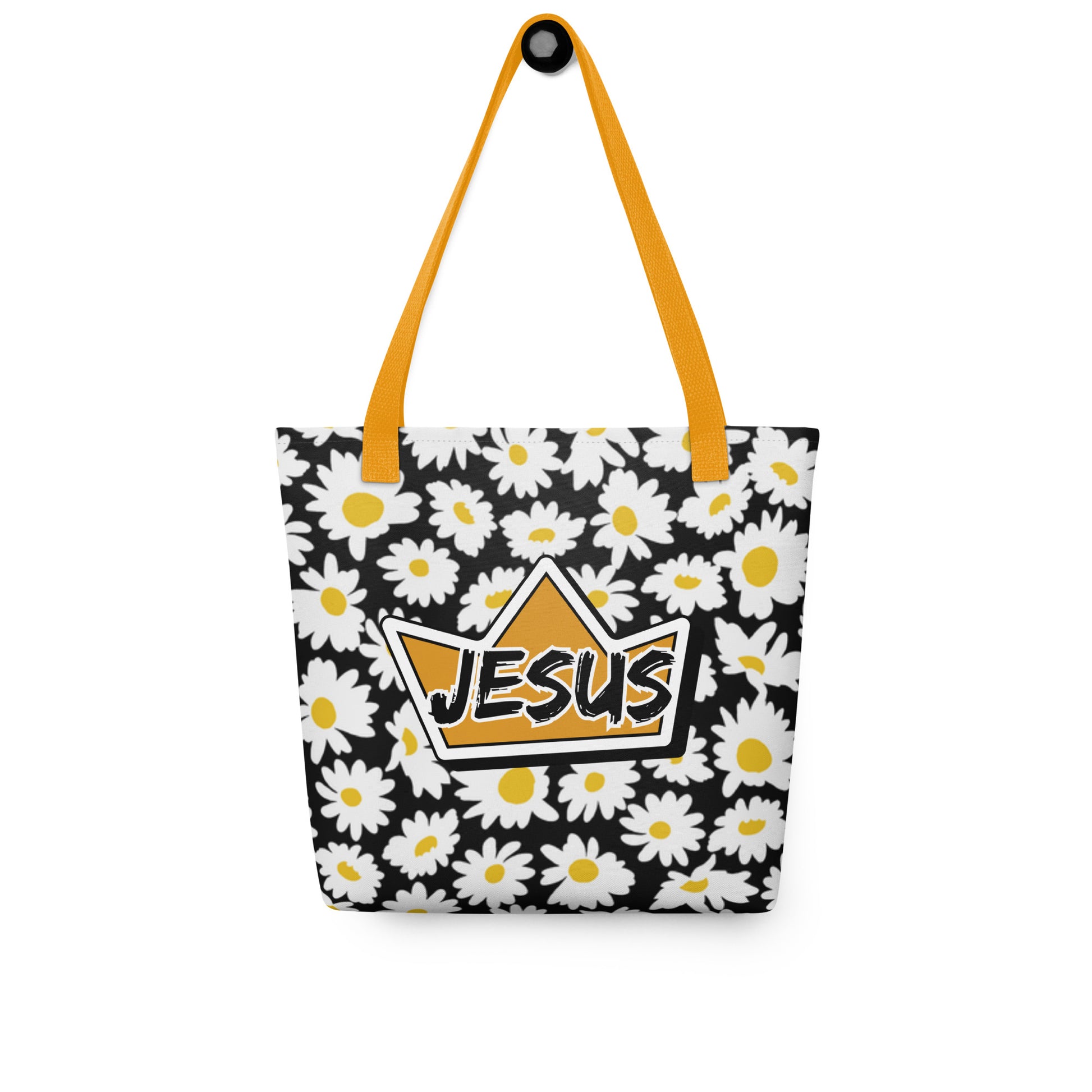 Black daisy-print tote bag with mustard yellow straps hanging on a hook, displaying the crown graphic with “JESUS” on the front.