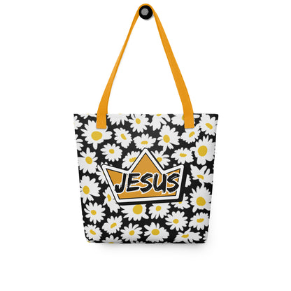Black daisy-print tote bag with mustard yellow straps hanging on a hook, displaying the crown graphic with “JESUS” on the front.