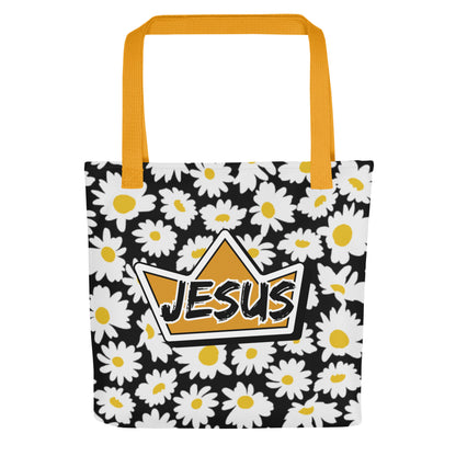 Front view of a black daisy-print tote bag with mustard yellow straps, featuring a gold crown graphic with the word “JESUS” in bold lettering on the front.