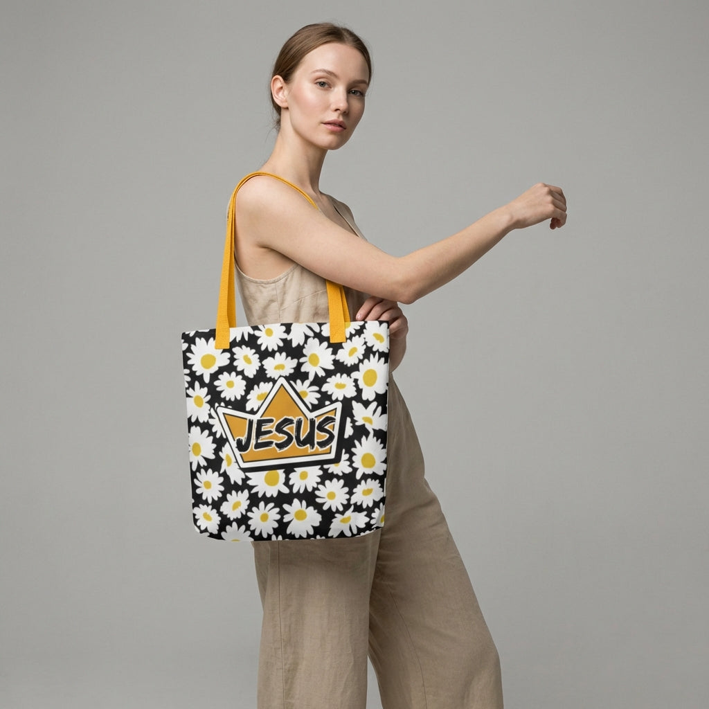Model carrying a black daisy-print tote with mustard yellow straps, featuring a crown-shaped “JESUS” design on the front.