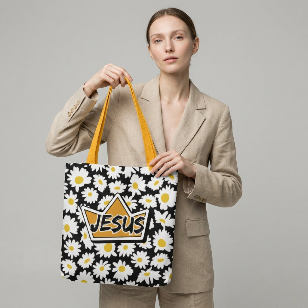 Model carrying a black daisy-print tote with mustard yellow straps, featuring a crown-shaped “JESUS” design on the front.
