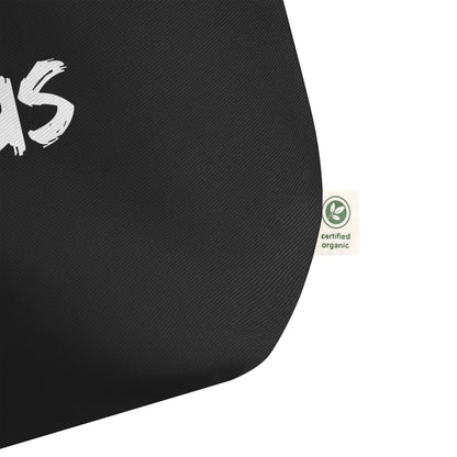 Close-up of the black cotton tote fabric, showing the textured weave and a side “certified organic” tag detail.