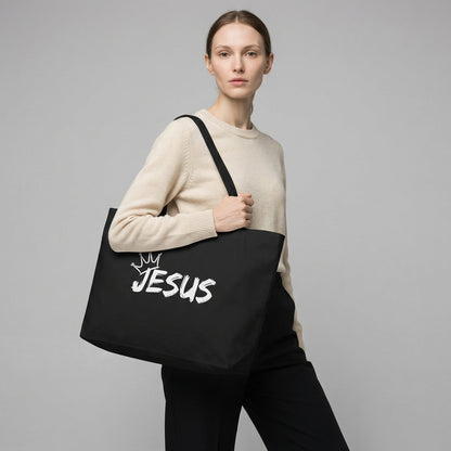 Model holding a large black cotton tote bag with a white “JESUS” graphic and crown detail on the front.