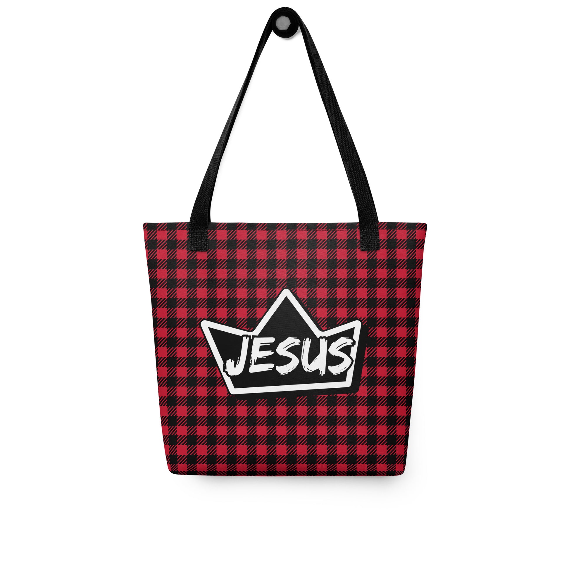 Red and black plaid tote bag with black straps hanging on a hook, displaying a black crown graphic with “JESUS” in white text.