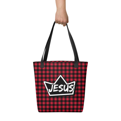 Tote bag held by hand with black straps, featuring a red and black buffalo check pattern and a bold crown emblem with “JESUS” across the center.