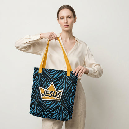 Model holding a tote bag with yellow handles, a blue-and-black zebra pattern, and a gold crown “JESUS” graphic on the front.