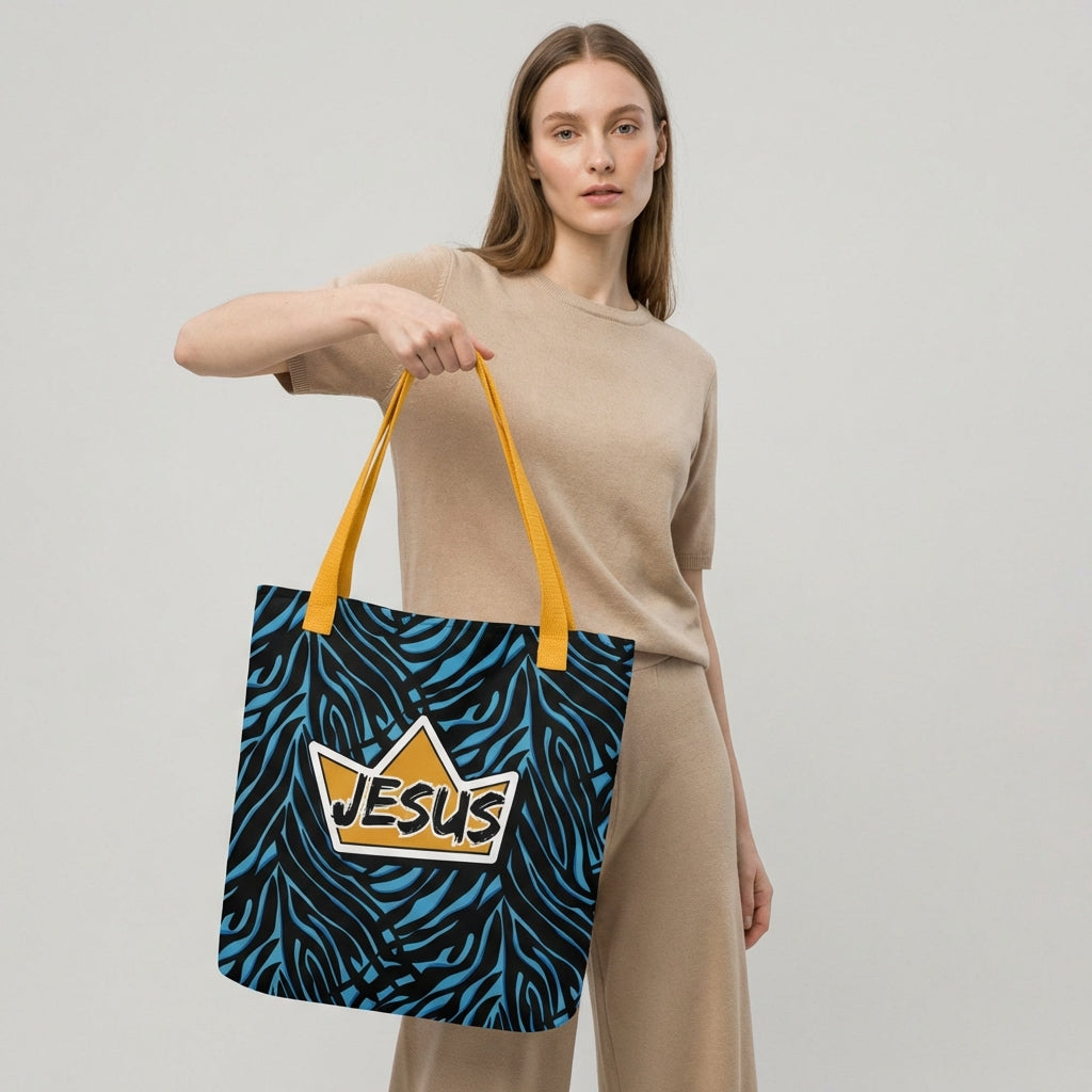 Model holding a tote bag with yellow handles, a blue-and-black zebra pattern, and a gold crown “JESUS” graphic on the front.