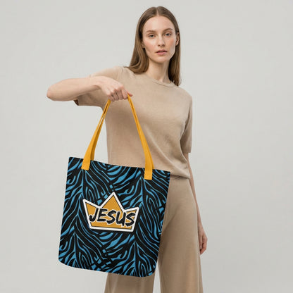 Model holding a tote bag with yellow handles, a blue-and-black zebra pattern, and a gold crown “JESUS” graphic on the front.