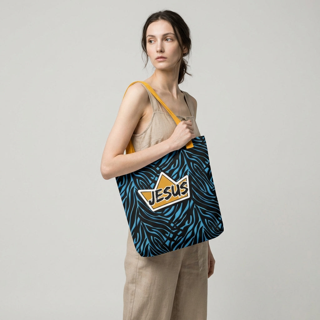 Model holding a tote bag with yellow handles, a blue-and-black zebra pattern, and a gold crown “JESUS” graphic on the front.