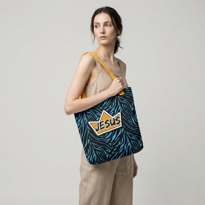 Model holding a tote bag with yellow handles, a blue-and-black zebra pattern, and a gold crown “JESUS” graphic on the front.