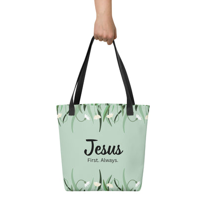 Tote bag held by hand with black straps, featuring a mint green floral pattern and the words “Jesus. First. Always.”