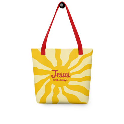 Tote bag hanging on a hook with red handles, yellow sunburst background, and “Jesus First. Always.” text.