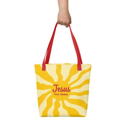 Hand holding red-handle tote bag with yellow sunburst design and “Jesus First. Always.” message.