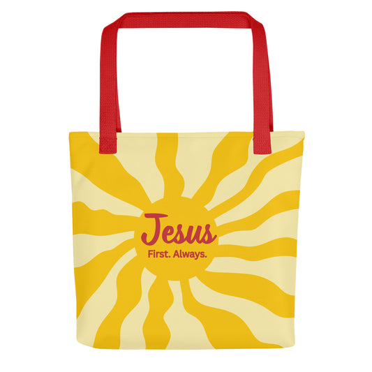 Front view of tote bag with red straps and yellow sunburst design, featuring the words “Jesus First. Always.”