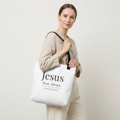 Model holding a white tote bag that reads “Jesus First. Always.” in dark gray with “Matthew 6:33.”