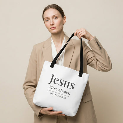 Model holding a white tote bag that reads “Jesus First. Always.” in dark gray with “Matthew 6:33.”