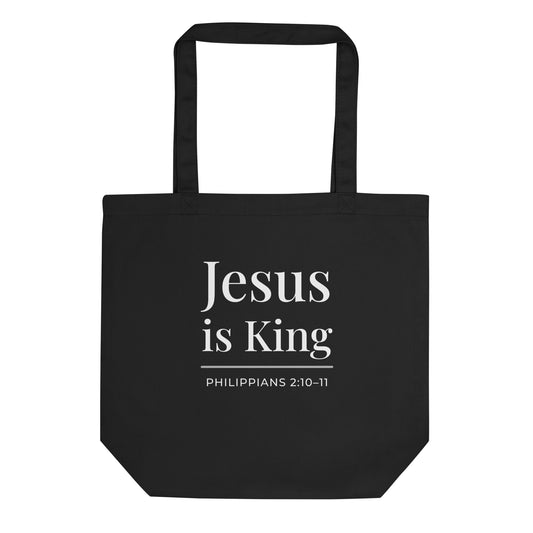 Black tote bag with white text reading “Jesus is King” and “Philippians 2:10–11” on the front.