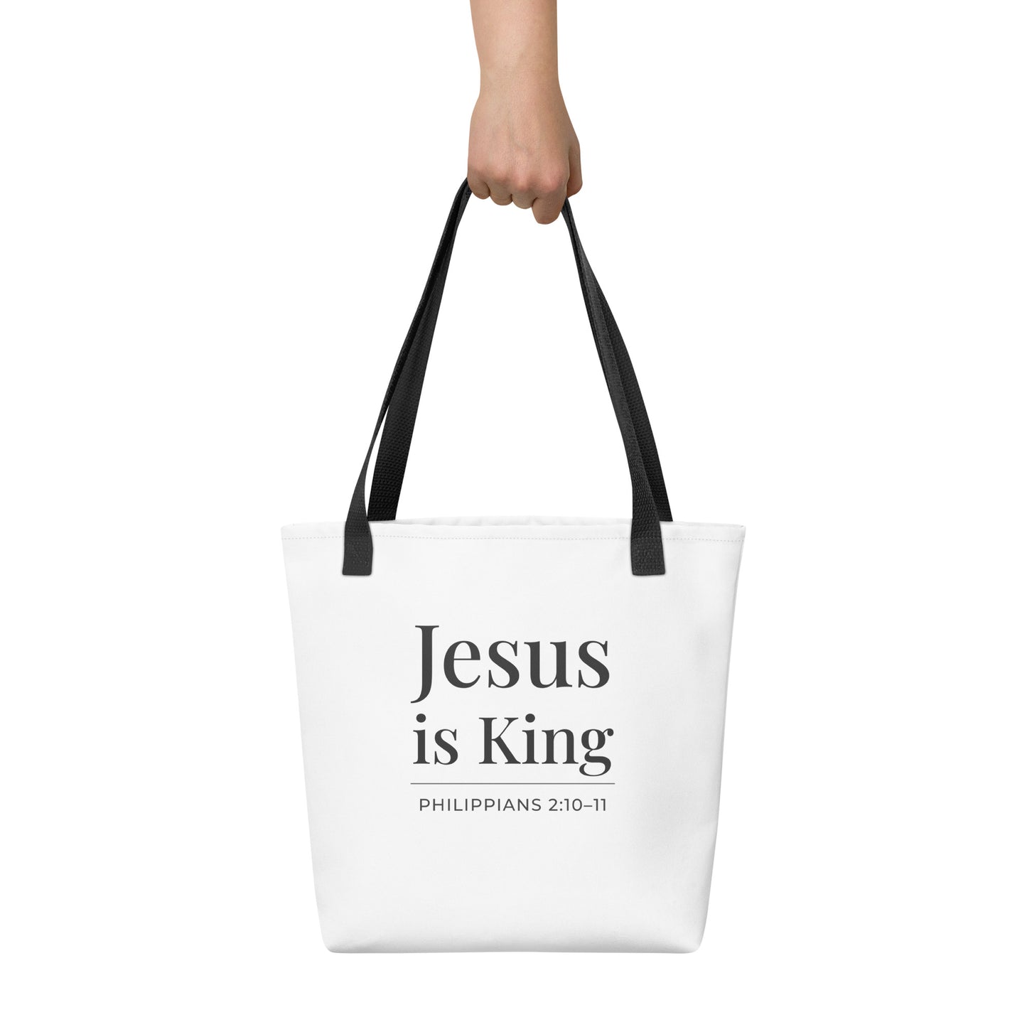 White tote bag held in hand featuring “Jesus is King” in dark gray text with “Philippians 2:10–11” beneath.