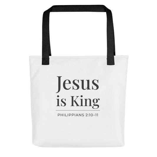 White tote bag with black handles featuring “Jesus is King” and “Philippians 2:10–11” in dark gray text.