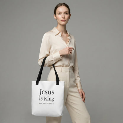 Model holding a white tote bag with dark gray “Jesus is King” and the verse reference “Philippians 2:10–11.”