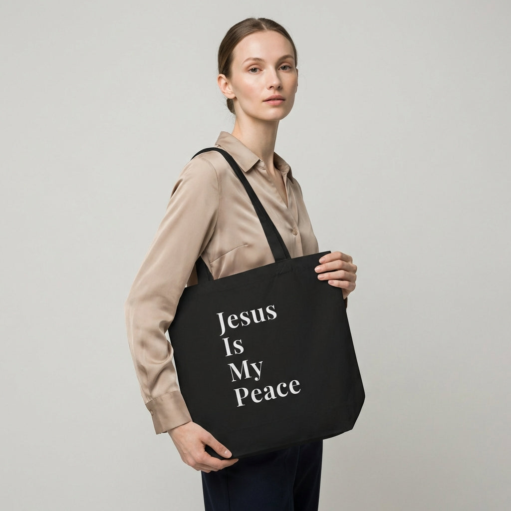 Model holding a black cotton tote bag featuring white “Jesus Is My Peace” text.