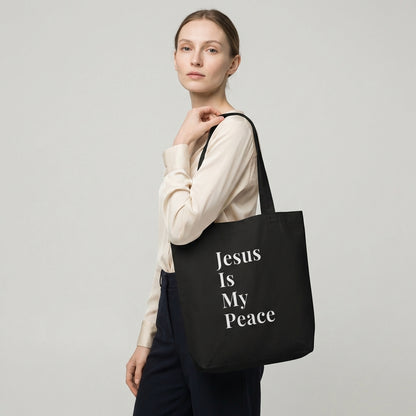 Model holding a black cotton tote bag featuring white “Jesus Is My Peace” text.