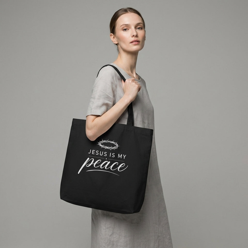 Model carrying a black cotton Christian tote bag with a white “Jesus Is My Peace” faith-based design.