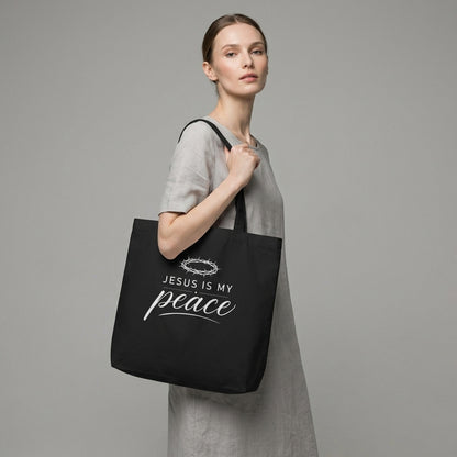 Model carrying a black cotton Christian tote bag with a white “Jesus Is My Peace” faith-based design.