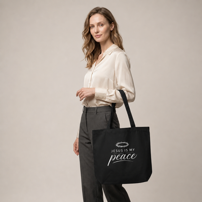 Model carrying a black cotton Christian tote bag with a white “Jesus Is My Peace” faith-based design.