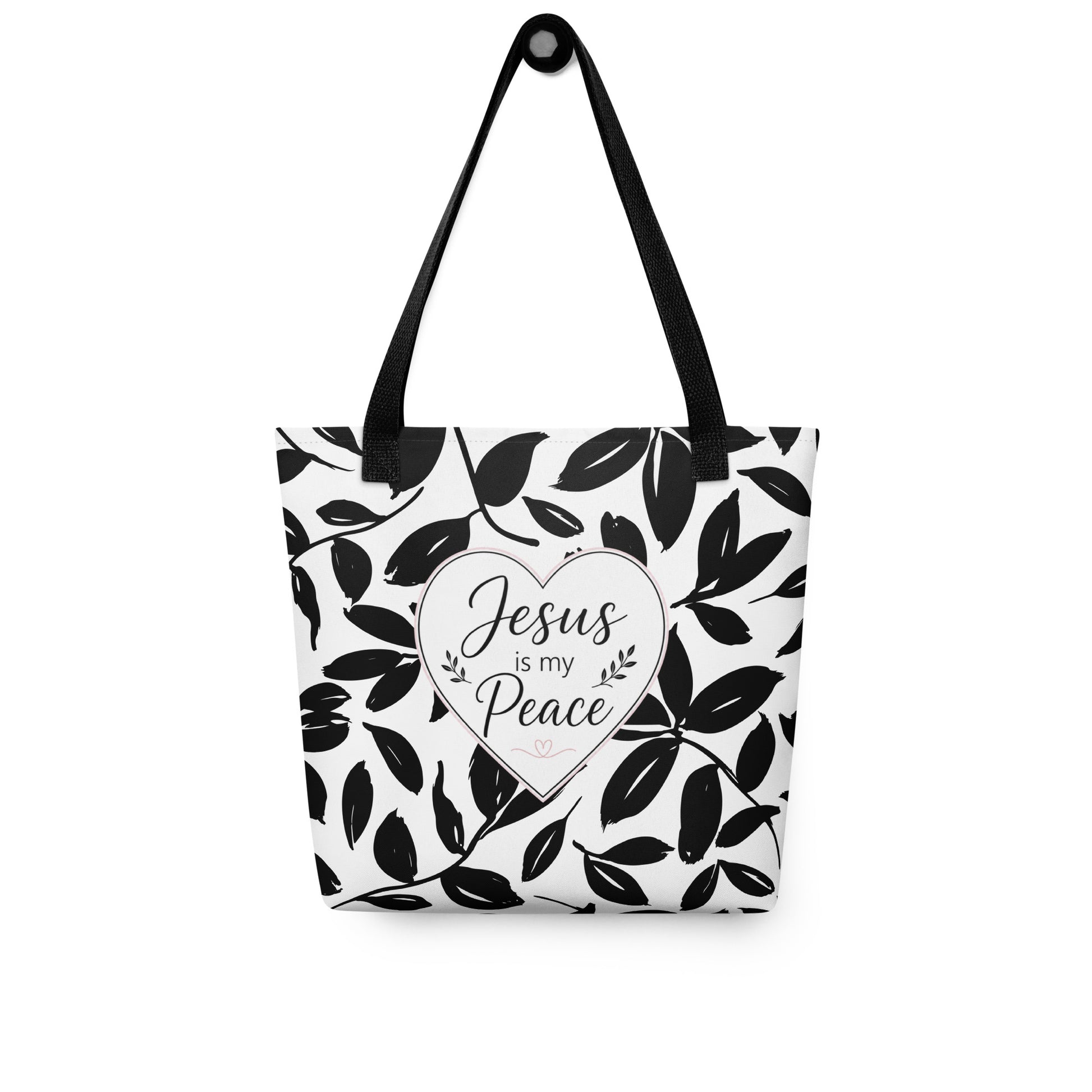Christian tote bag hanging on a hook, featuring black straps, black and white leaf print, and a heart-shaped “Jesus is my Peace” design.