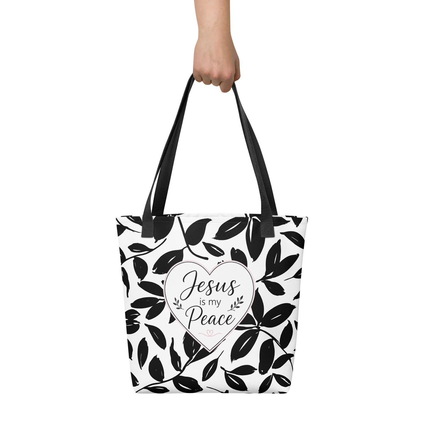 Person holding a black and white Christian tote bag with black handles, leafy print, and “Jesus is my Peace” lettering.