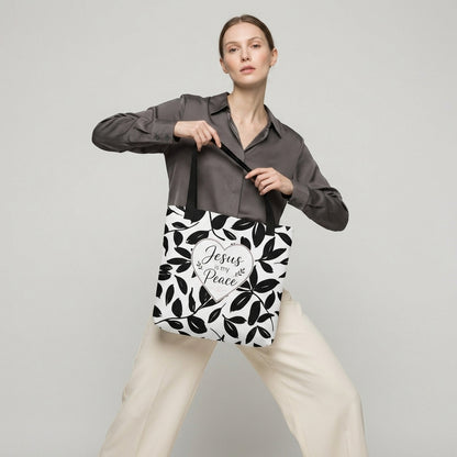 Model carrying a black and white Christian tote bag with black handles, leafy artwork, and a “Jesus is my Peace” heart design.