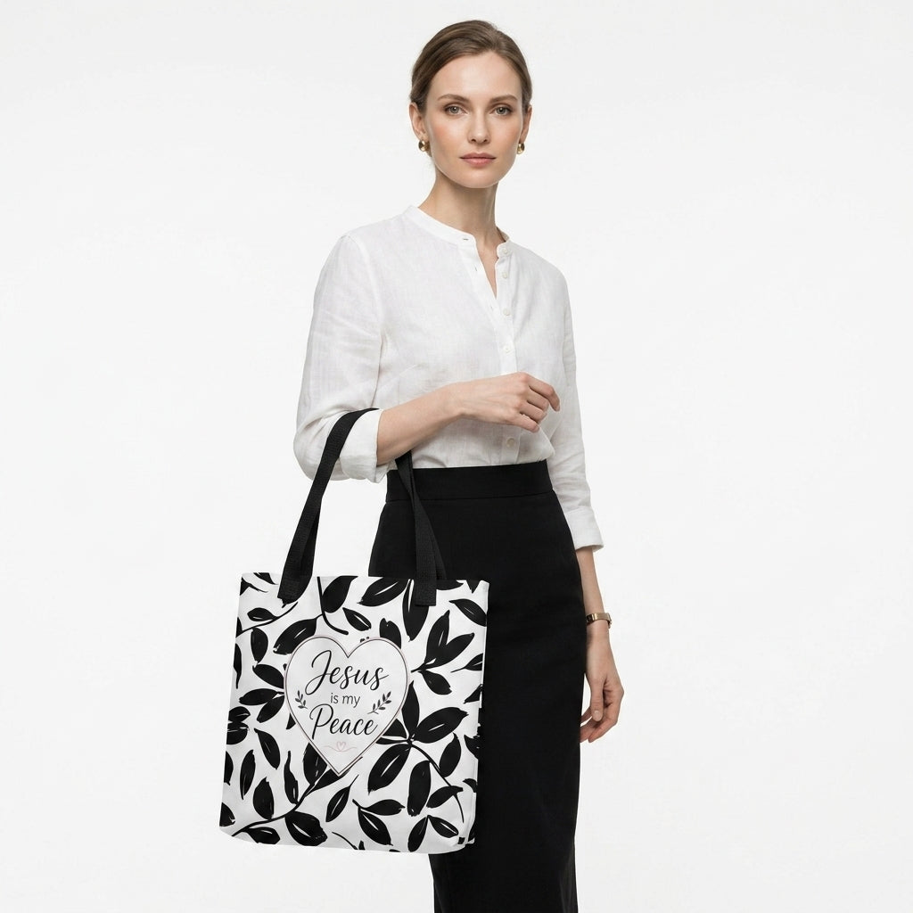 Model carrying a black and white Christian tote bag with black handles, leafy artwork, and a “Jesus is my Peace” heart design.