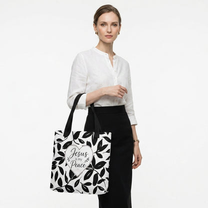 Model carrying a black and white Christian tote bag with black handles, leafy artwork, and a “Jesus is my Peace” heart design.